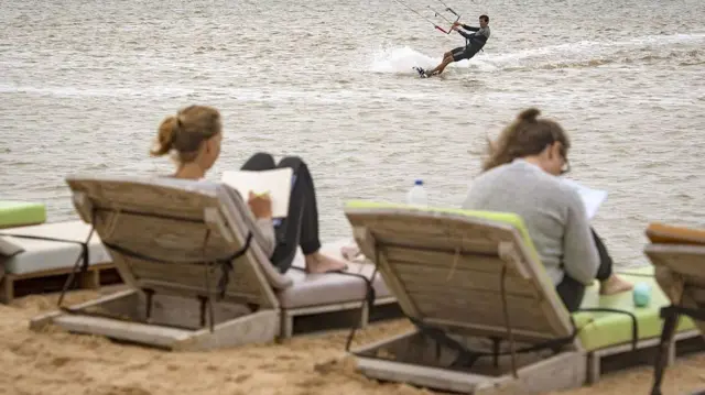 Deux vacanciers européens profitent de chaises longues au bord de la mer au Sahara occidental, tandis qu’un autre pratique le kitesurf